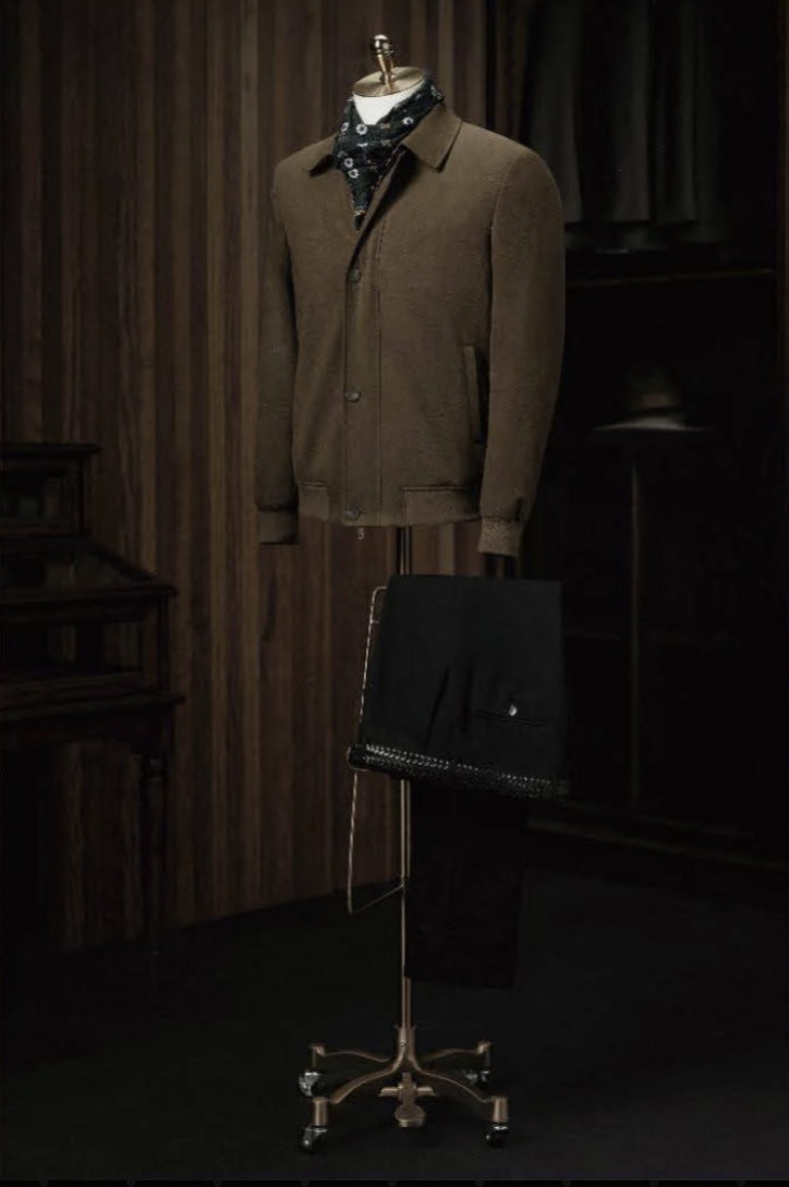 A dark brown casual jacket with a collar and 4-button fastening, displayed on a mannequin, with black trousers and a waistcoat in the background, set against a wooden background