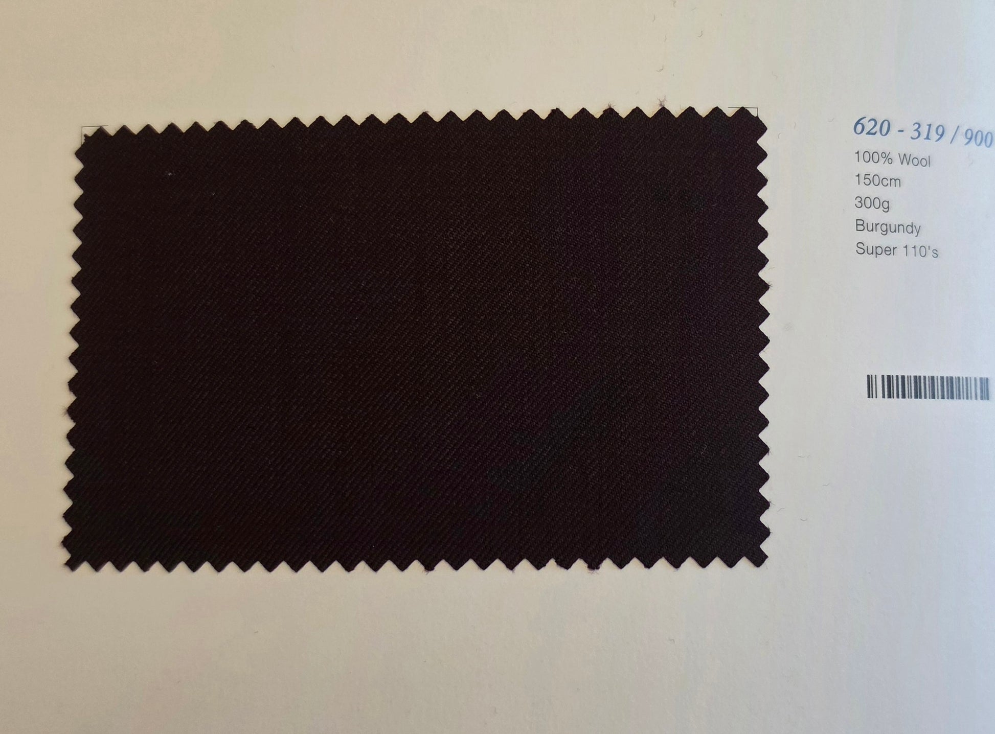 A dark burgundy wool fabric swatch with serrated edges, displayed on a white background next to printed specifications.