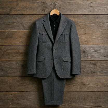 A dark gray wool suit set consisting of a two-button blazer and matching trousers, styled with a black collared shirt on a wooden hanger against a rustic brown wood plank background.