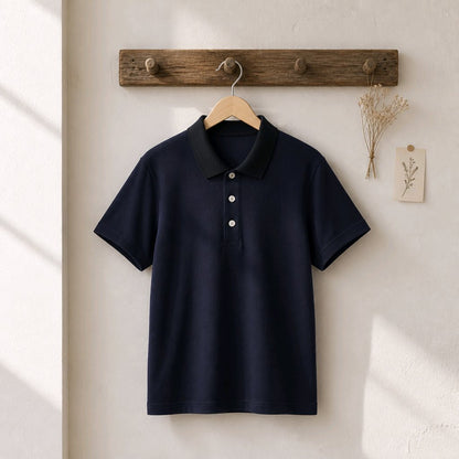 A dark navy blue short-sleeve polo shirt with a contrasting black collar and three white buttons, hanging on a wooden hanger from a rustic wooden peg rack against a textured off-white wall.