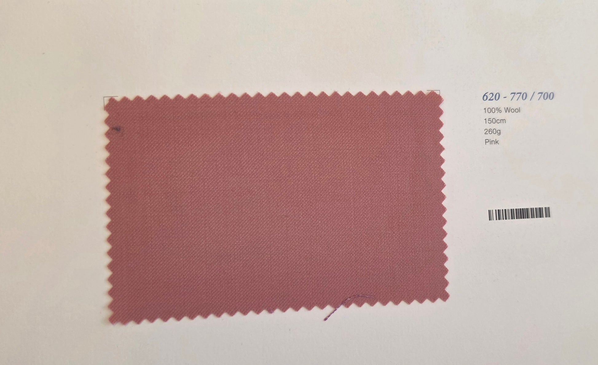 A fabric color swatch card showing a dusty rose pink woven material with a serrated edge, labeled with text on the right side including '620 - 770 / 700', '100% Wool', '150m', '280g', and 'Pink'.