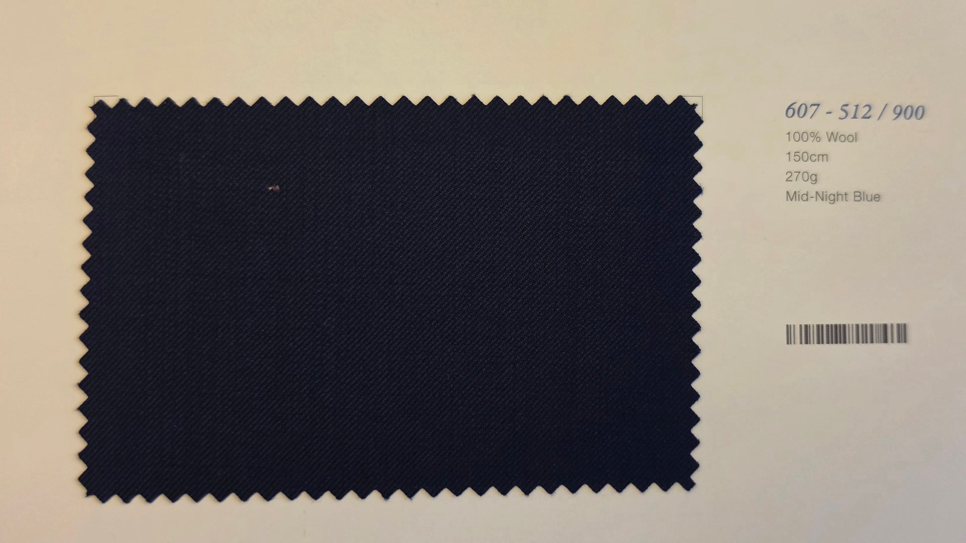 A fabric color swatch of Mid-Night Blue wool, showing a dark navy blue textured weave with zigzag-cut edges, displayed on a light beige background with product details printed on the right.