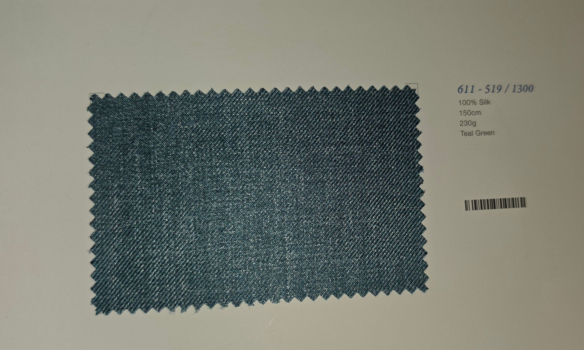 A fabric swatch card displaying a textured teal green woven material with zigzag-cut edges, labeled with code 611-519/1300 and weight 200g on a plain light background.