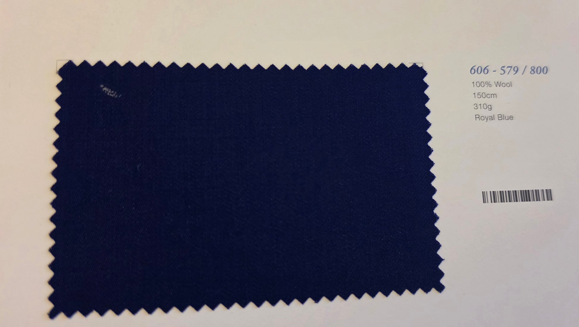 A fabric swatch card showing a dark royal blue wool material with zigzag-cut edges, alongside printed text including the code 606-579/800, 100% Wool, 150cm, 31kg, and Royal Blue.