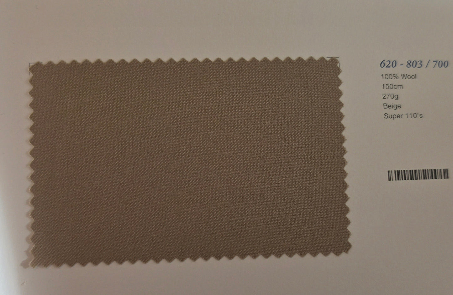 A fabric swatch card showing a rectangular beige wool sample with serrated edges, alongside printed text including color code 620-803/700, 100% Wool, 150cm, 270g, Beige, and Super 110's.