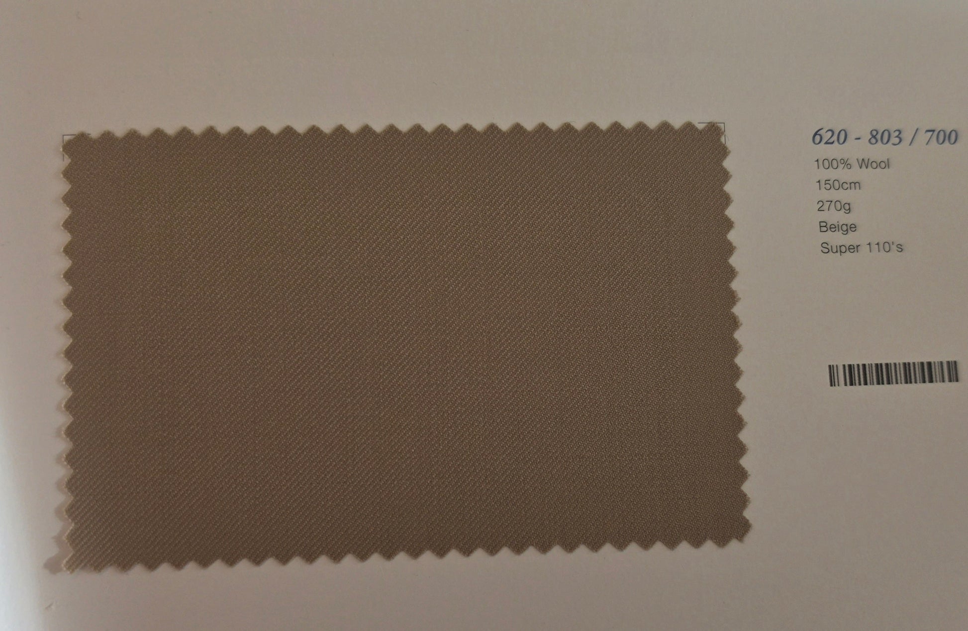 A fabric swatch card showing a rectangular beige wool sample with serrated edges, alongside printed text including color code 620-803/700, 100% Wool, 150cm, 270g, Beige, and Super 110's.