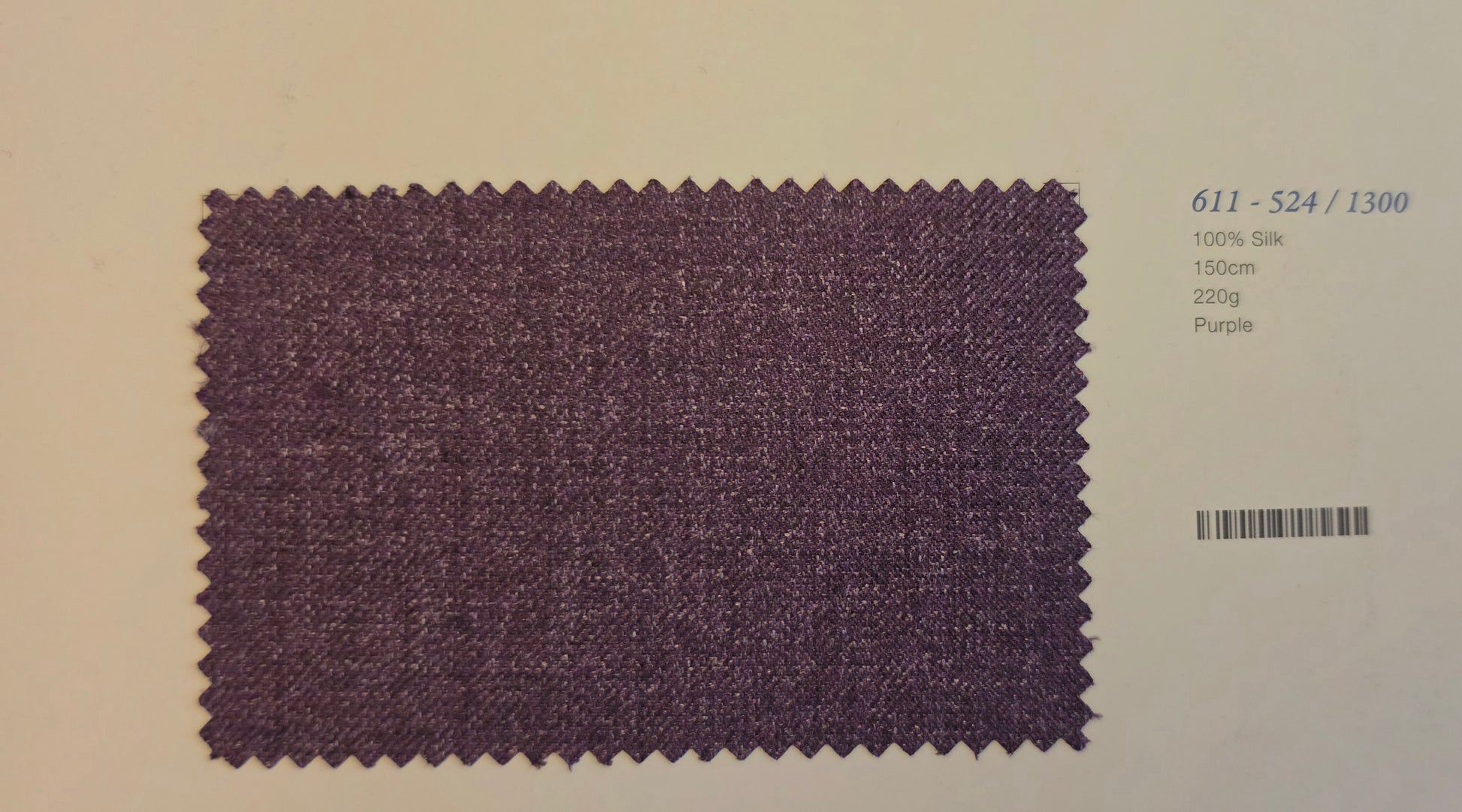 A fabric swatch card showing a textured purple silk material sample with zigzag-cut edges, alongside printed text including the code '611 - S24 / 1300' and '100% Silk 150m 220g Purple'.