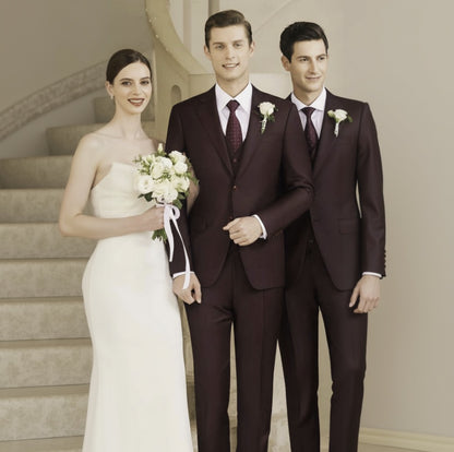 A group of three men in burgundy suits with notched lapels and a woman in a white gown holding a bouquet, standing on stairs.