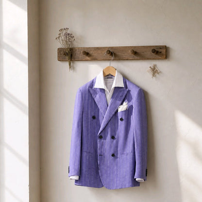 A lavender purple double-breasted pinstripe blazer with a white striped shirt and white pocket square, hanging on a wooden coat rack against a textured beige wall.
