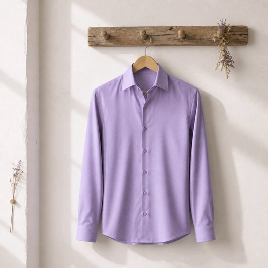 A lavender purple long-sleeve button-down dress shirt hanging on a wooden hanger from a rustic wooden wall hook, set against a warm off-white wall with soft sunlight shadows.