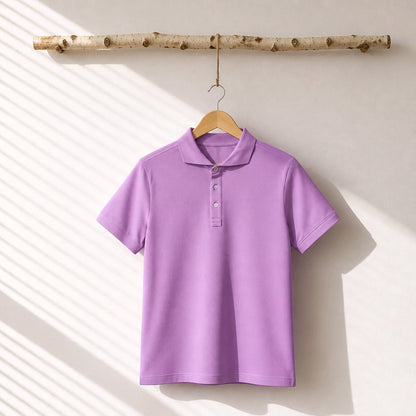 A lavender purple short-sleeve polo shirt hanging on a wooden hanger from a birch branch, set against a warm off-white wall with soft diagonal window shadow stripes.