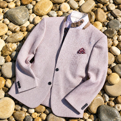 A light beige textured blazer with black buttons, styled on a bed of smooth river stones. The blazer is shown with a white patterned dress shirt, a red patterned pocket square, and a brown leather pocket clip.