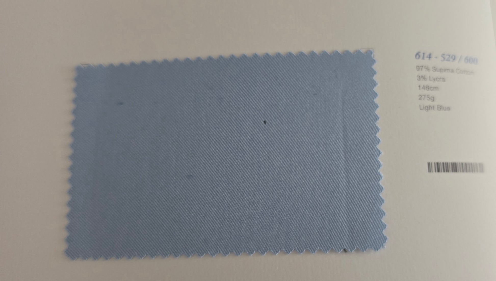 A light blue fabric color swatch with serrated edges, placed on a white background next to printed color information.