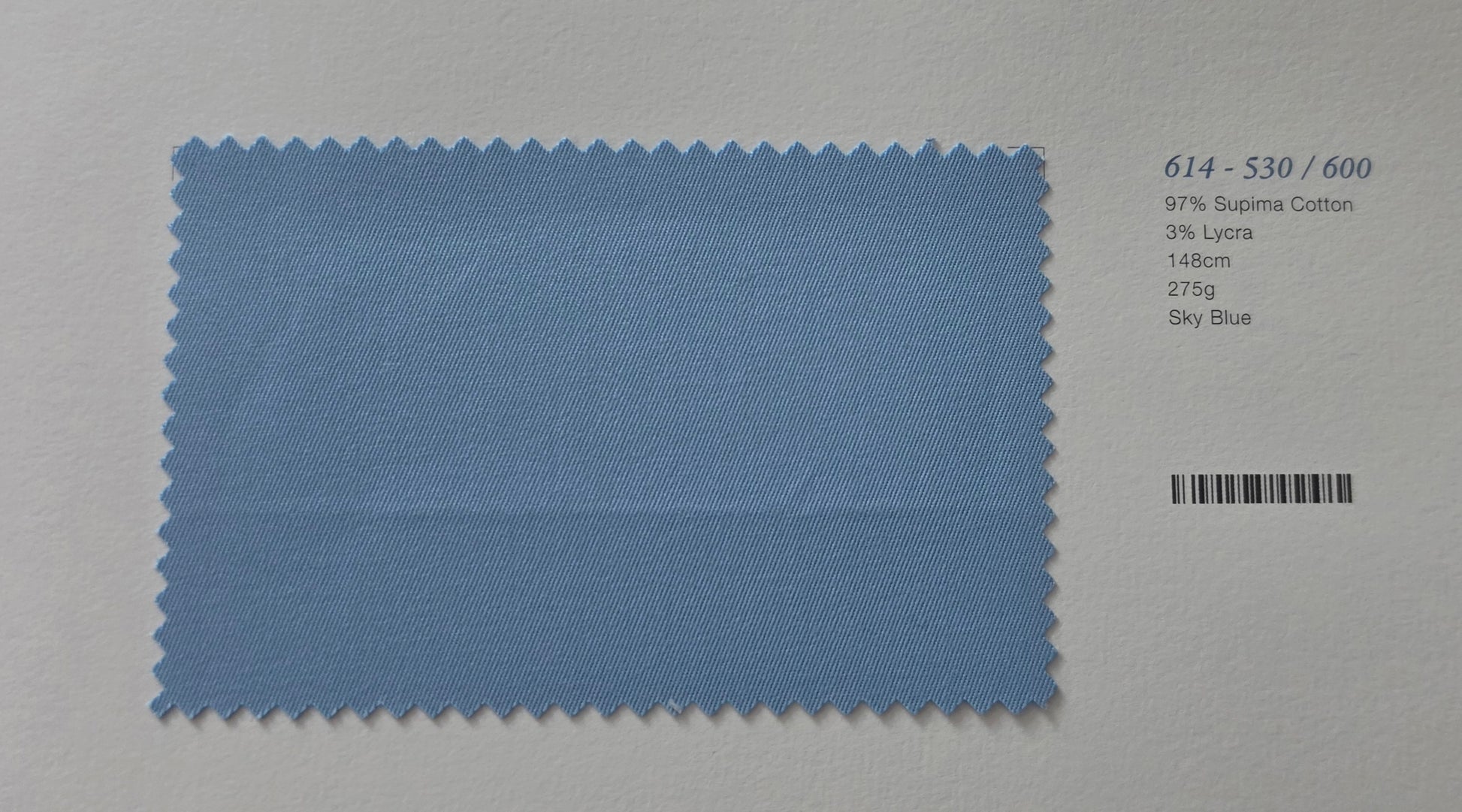 A light blue fabric swatch with serrated edges on a white background, next to printed text showing color code 614-530/600 and fabric details, with a barcode on the right.