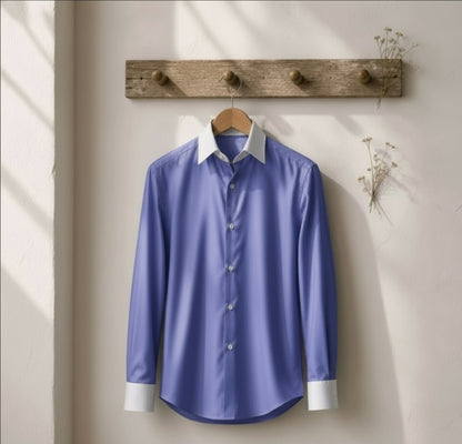 A light blue long-sleeve button-up shirt with a white collar and white cuffs, hanging on a wooden hanger from a rustic wooden peg rack against a beige wall.
