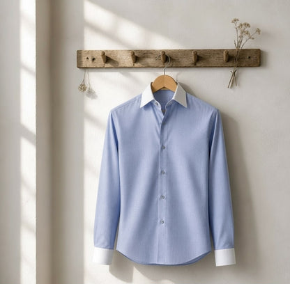 A light blue long-sleeve dress shirt with a contrasting white collar and white cuffs, hanging on a wooden hanger from a rustic wooden wall rack against a warm off-white wall.