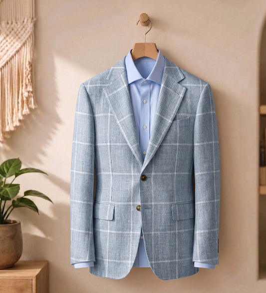 A light blue windowpane plaid blazer jacket styled over a matching light blue dress shirt, hanging on a wooden hanger against a warm beige wall.