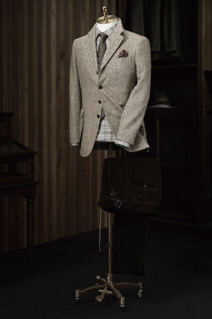 A light brown herringbone tweed jacket and green herringbone trousers displayed on a mannequin against a wooden background.