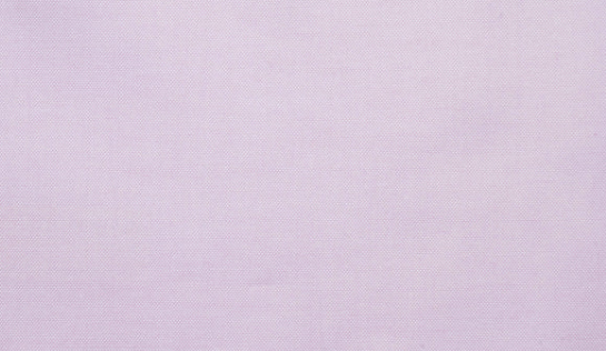 A light pink long-sleeve button-up shirt hanging on a wooden hanger from a rustic wooden wall hook, set against a textured off-white wall with soft window shadow patterns.