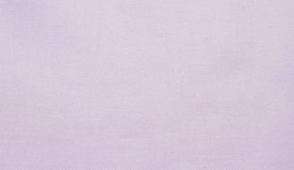 A light pink long-sleeve button-up shirt hanging on a wooden hanger from a rustic wooden wall hook, set against a textured off-white wall with soft window shadow patterns.