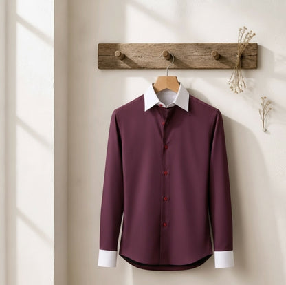 A long-sleeve button-up dress shirt in deep burgundy with a contrasting white collar and white cuffs, hanging on a wooden hanger from a rustic wooden wall hook.