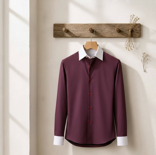 A long-sleeve button-up dress shirt in deep burgundy with a contrasting white collar and white cuffs, hanging on a wooden hanger from a rustic wooden wall hook.