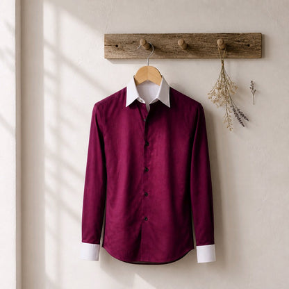 A long-sleeve button-up shirt in deep burgundy with a contrasting white collar and white cuffs, hanging on a wooden hanger from a rustic wooden peg rack against a textured off-white wall.