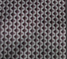 A long-sleeve button-up shirt with a small repeating geometric pattern in dark brown and muted purple, hanging on a wooden hanger from a rustic wooden peg on a textured off-white wall.