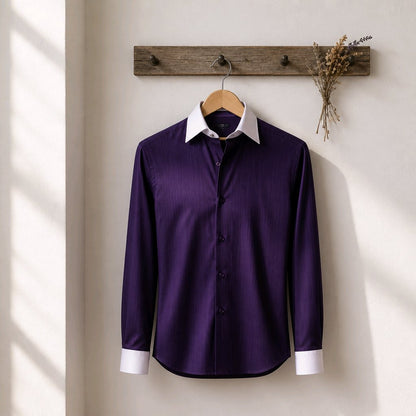 A long-sleeve purple dress shirt with a white collar and white cuffs, hanging on a wooden hanger from a rustic wooden wall hook with dried flowers.