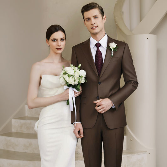 A man and a woman standing next to each other, the woman holding a bouquet, both dressed in brown single-breasted suits with notched lapels and double vents.