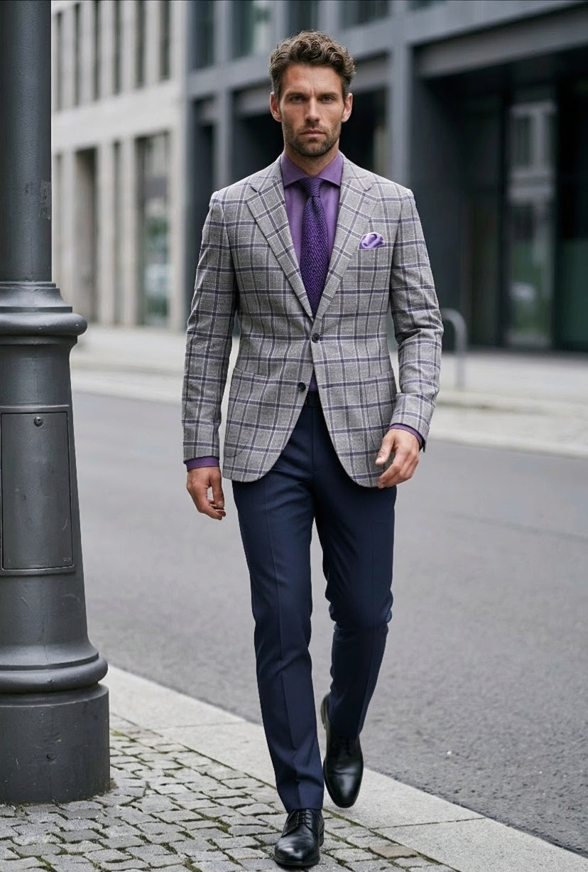 A man walking on a city street wearing a gray and white windowpane plaid blazer, a purple shirt and tie, navy trousers, and black dress shoes.