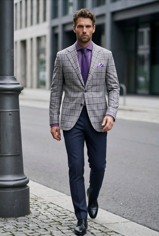 A man walking on a city street wearing a gray and white windowpane plaid blazer, a purple shirt and tie, navy trousers, and black dress shoes.
