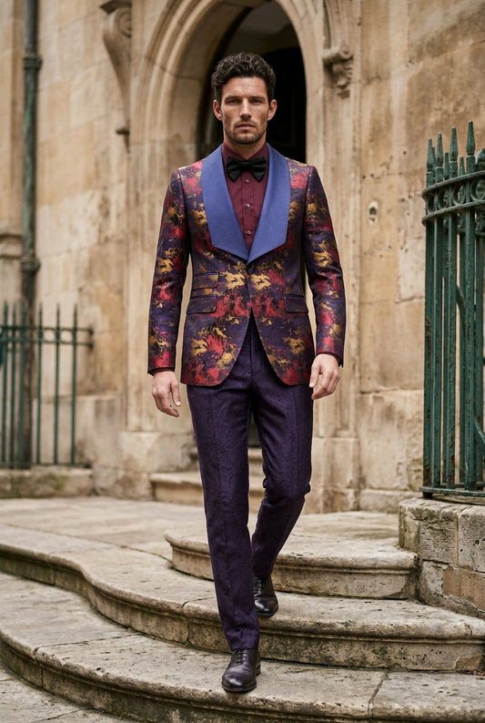 A man walks down stone steps wearing a tailored suit with a heavily patterned floral jacket featuring blue shawl lapels, matching trousers, a dark bow tie, and a blue shirt.