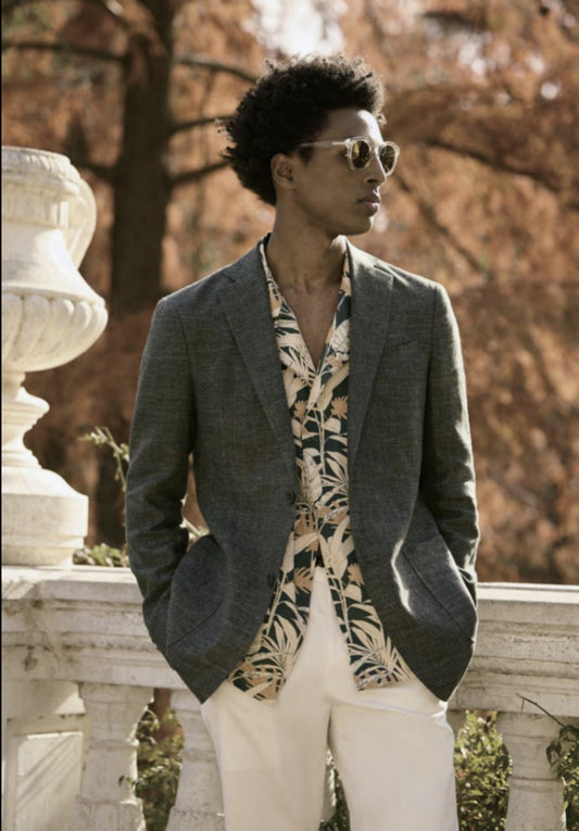 A man wearing a Italian green linen-cotton jacket with a notched lapel and dark brown buttons, paired with white trousers and a white paisley shirt.