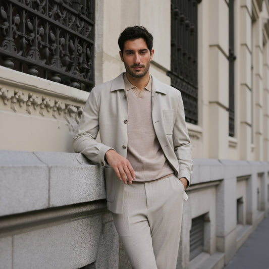 A man wearing a beige Italian stone/cotton stretch two piece suit with light brown buttons, standing against an architectural background.