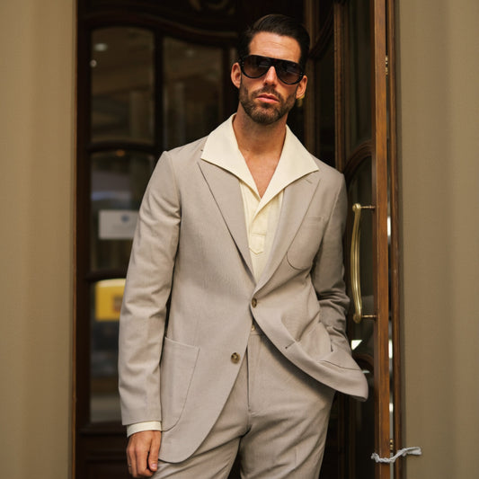 A man wearing a beige Italian stone two-piece suit with a notched lapel, patch breast pocket, and flapped pockets. The suit has light brown buttons and a matte finish.