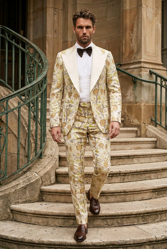 A man wearing a beige and gold patterned tuxedo with white shawl lapels, a white shirt, and a black bow tie walks down stone stairs.