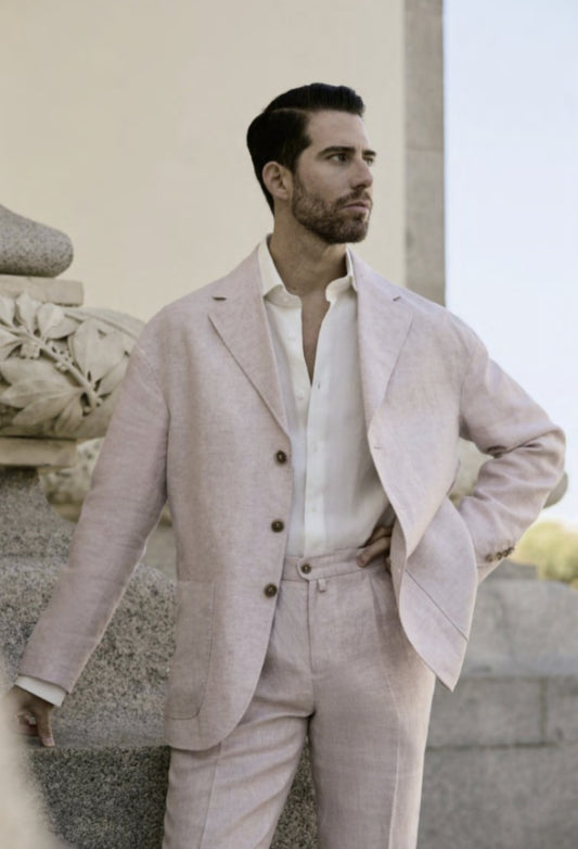 A man wearing a beige linen single breasted jacket with seven buttons and navy trousers.
