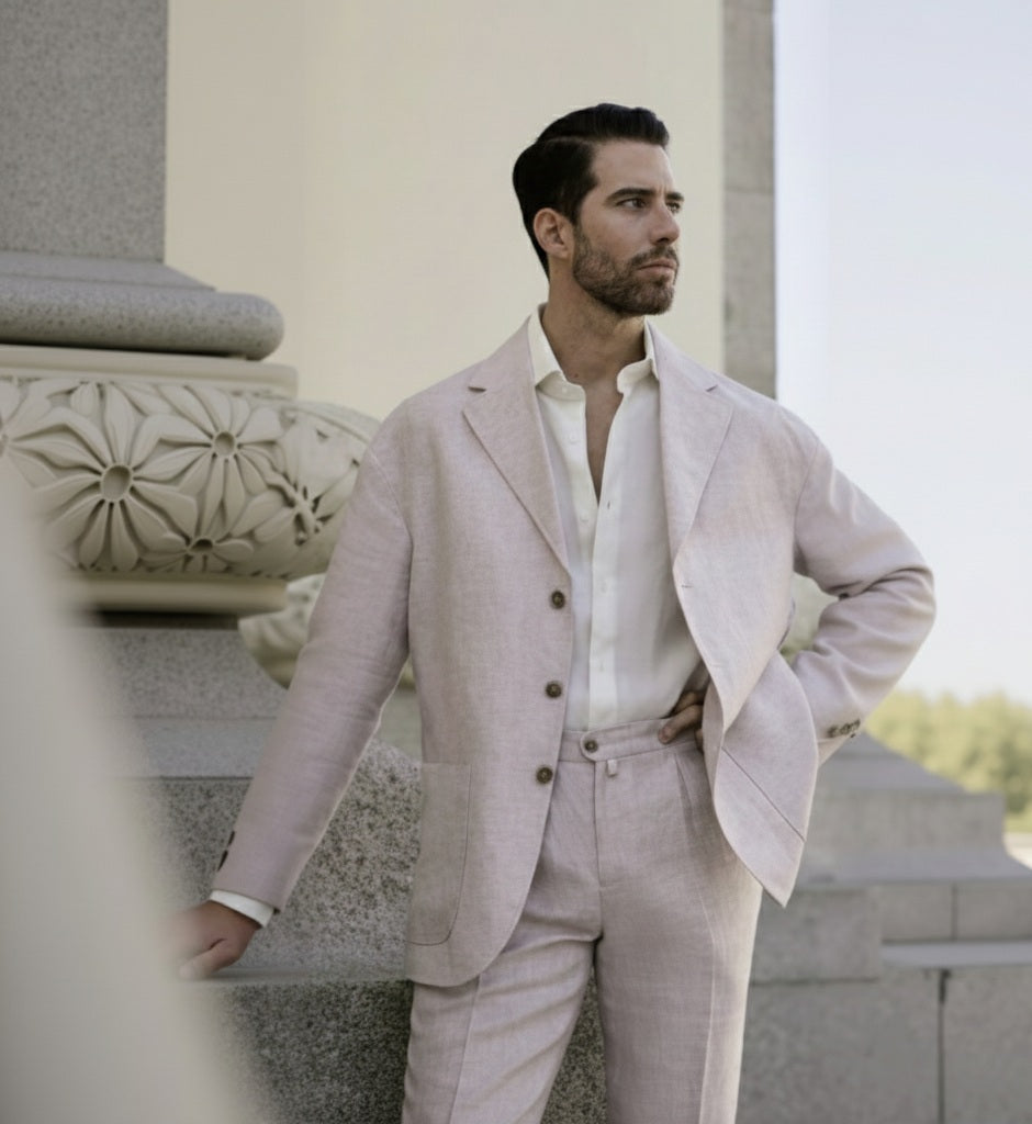 A man wearing a beige linen single breasted jacket with seven buttons and navy trousers.