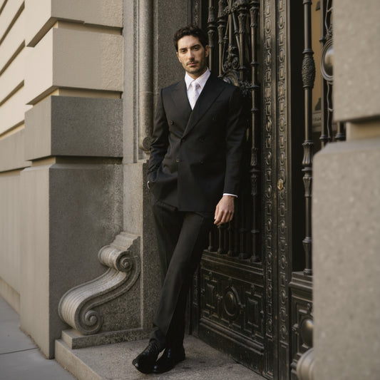 A man wearing a black double-breasted, wool-spandex two-piece suit standing near a decorative wall.
