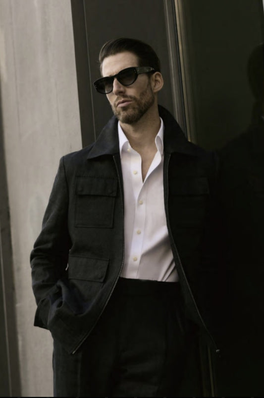 A man wearing a black linen herringbone zip-up jacket with matching trousers, standing outdoors.
