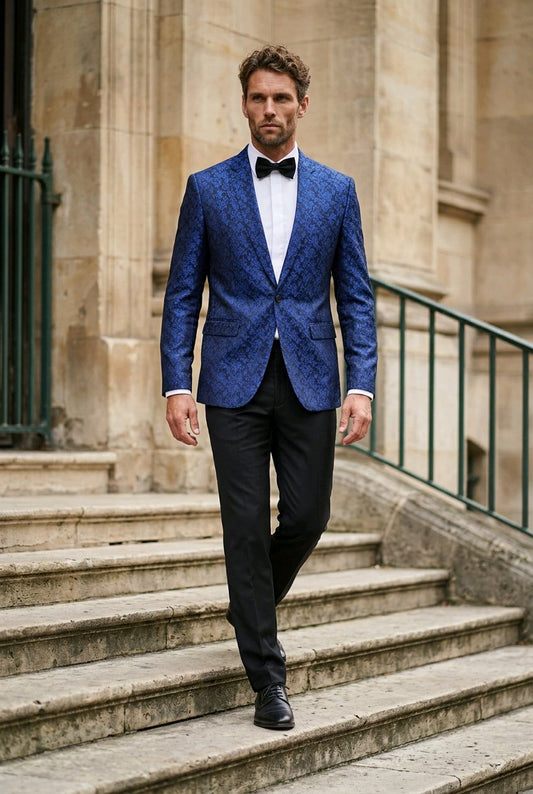 A man wearing a blue patterned blazer, black trousers, a white shirt, and a black bow tie walks down stone stairs in front of a classical stone building.