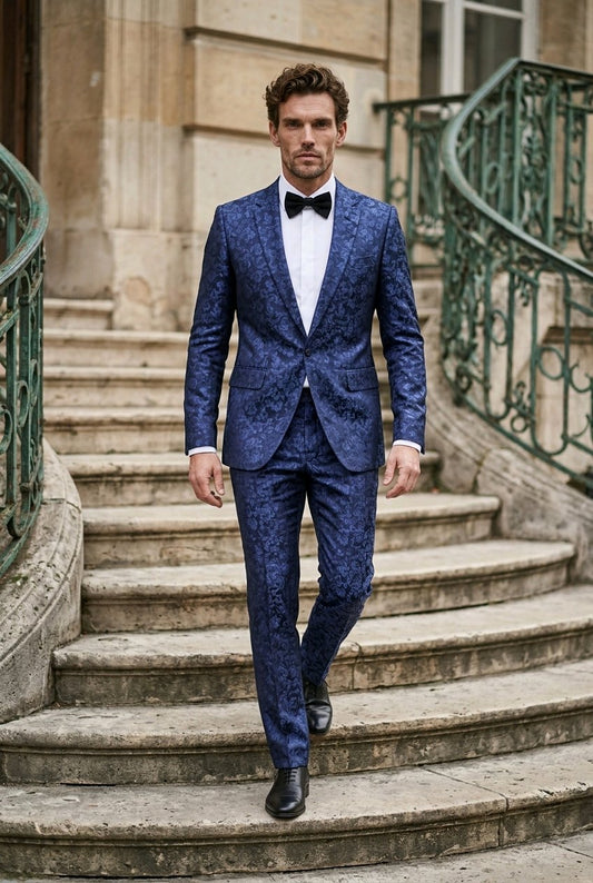 A man wearing a blue patterned suit with a white shirt and black bow tie walks down stone stairs in front of a building with green metal railings.