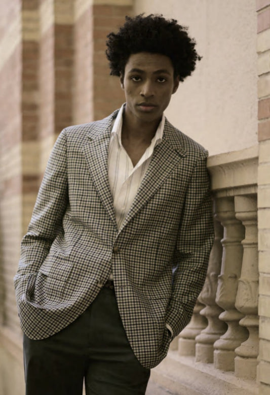 Person wearing a checkered blazer and white shirt against a stone wall background