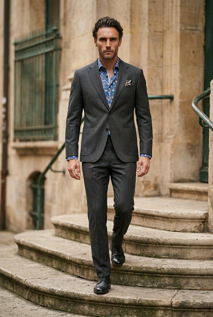 A man wearing a dark gray pinstripe suit, a blue patterned dress shirt, and black dress shoes walks down stone steps in front of a beige stone building.