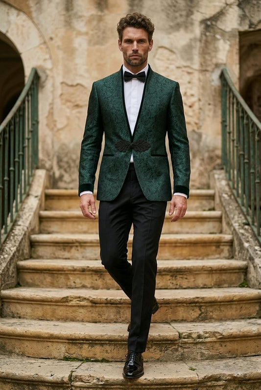 A man wearing a dark green textured patterned tuxedo jacket with black satin lapels, black trousers, a white shirt, and a black bow tie walks down stone stairs.