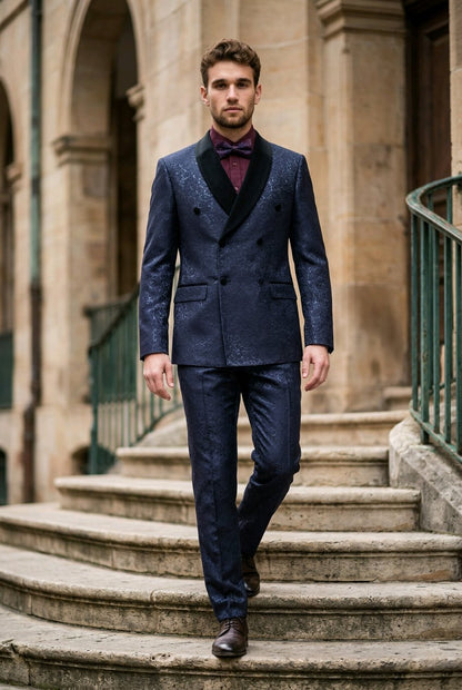 A man wearing a dark navy blue double-breasted suit with black shawl lapels, a burgundy bow tie, and brown dress shoes, walking down stone stairs in front of a historic stone building.