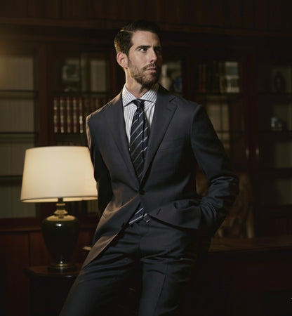 A man wearing a navy and grey two-piece wool suit with a notched lapel, slanted pockets, and double vent design.