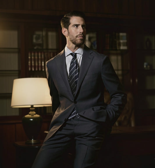 A man wearing a navy and grey two-piece wool suit with a notched lapel, slanted pockets, and double vent design.