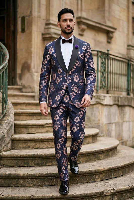A man wearing a navy blue floral-patterned suit with black peak lapels, a white shirt, a black bow tie, and a purple boutonniere, walking down stone steps in front of a historic building.